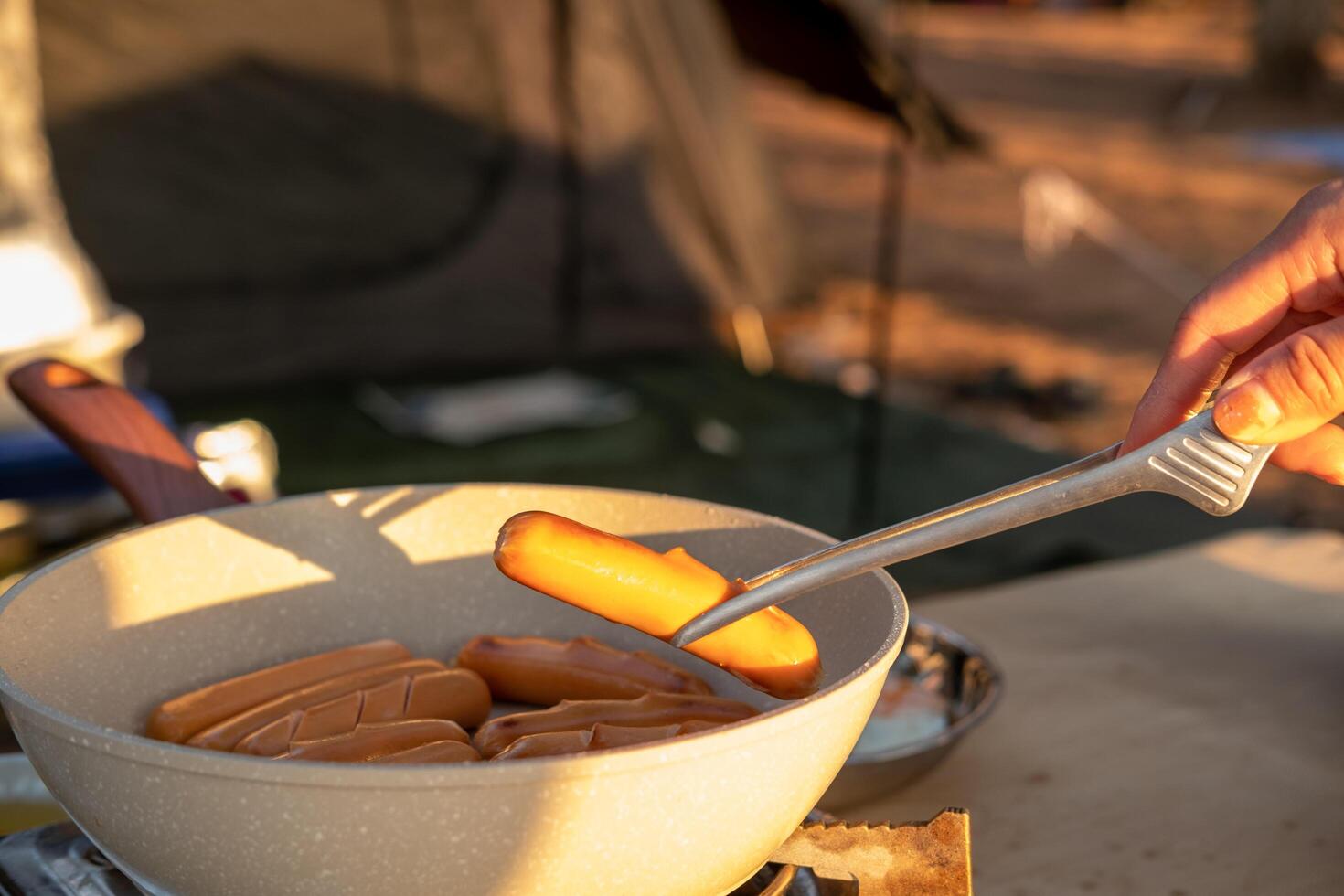 A woman's hand is holding sausages grilled on a pan. While going camping to relax photo