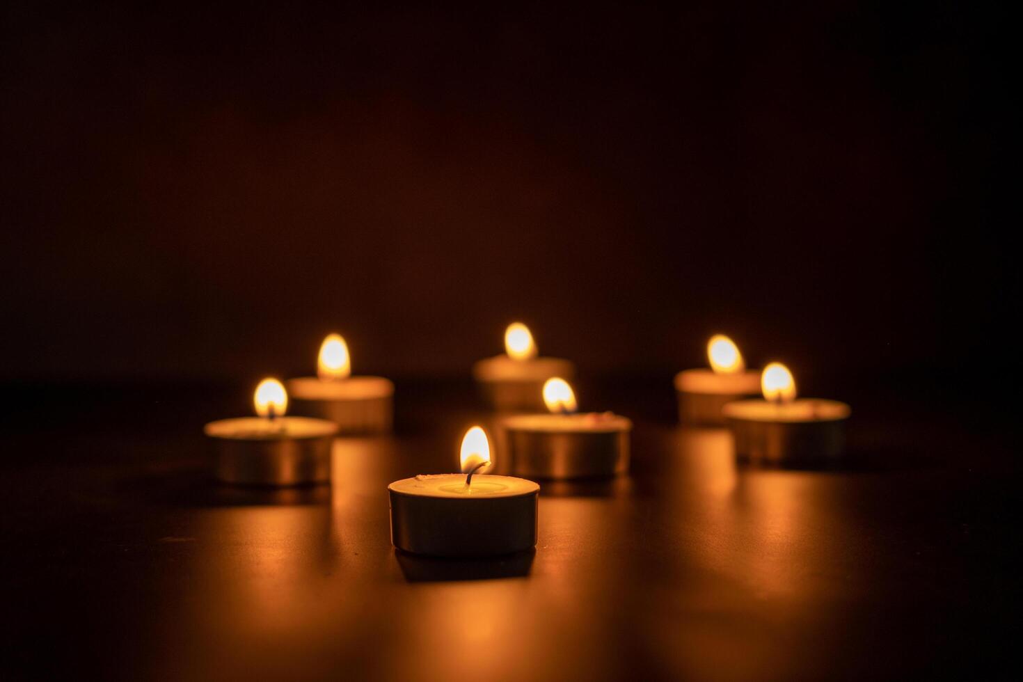 Many candles lit against a black background.Burning candles on dark tableMemory photo
