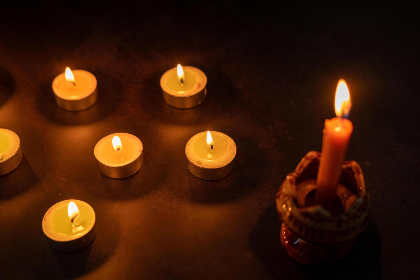 Many candles lit against a black background.Burning candles on dark tableMemory photo