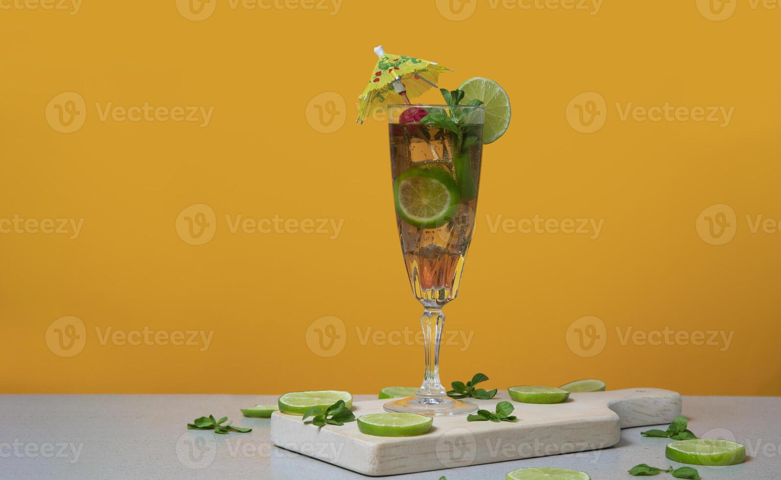 Cocktail in long glass filled with ice and lemon slices garnished with small yellow umbrellas, cherries and lemon slices on a wooden board photo