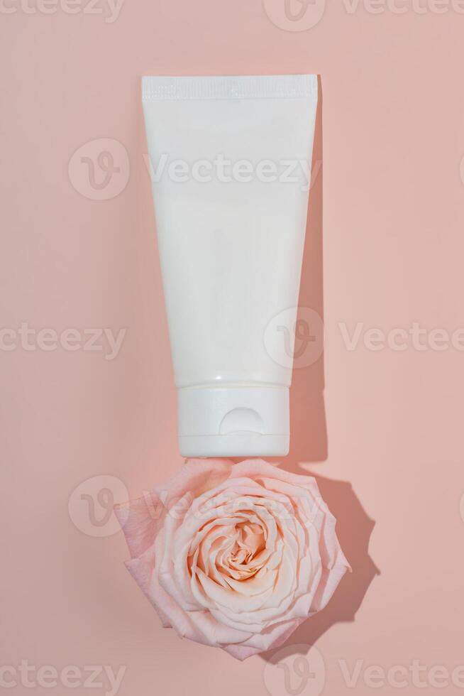 White unbranded tube for cosmetics with small pink roses and on pink background. Natural cosmetic product mock up, branding concept. photo