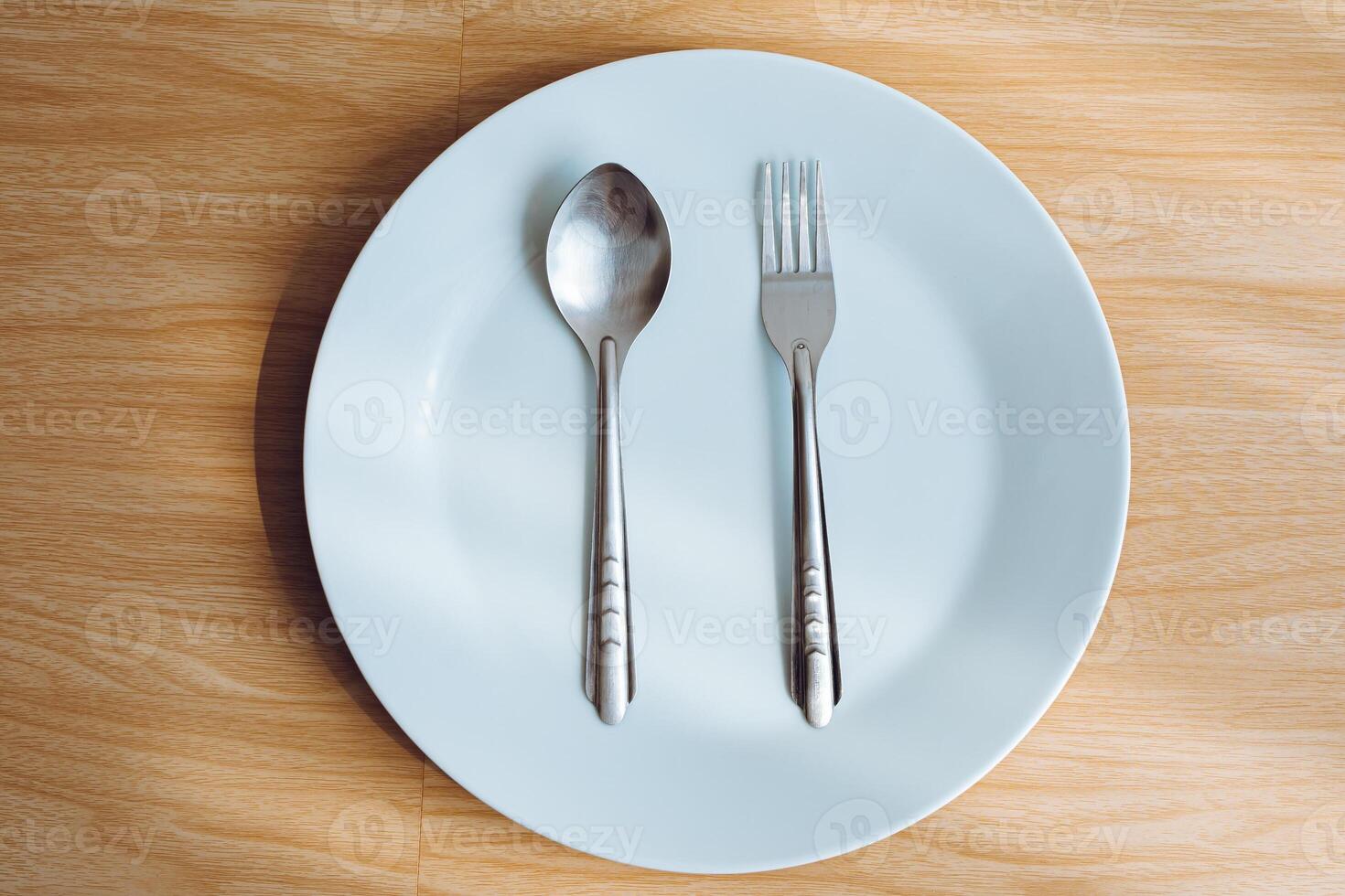 1 empty white plate and 1 pair of cutlery with a wooden background. photo