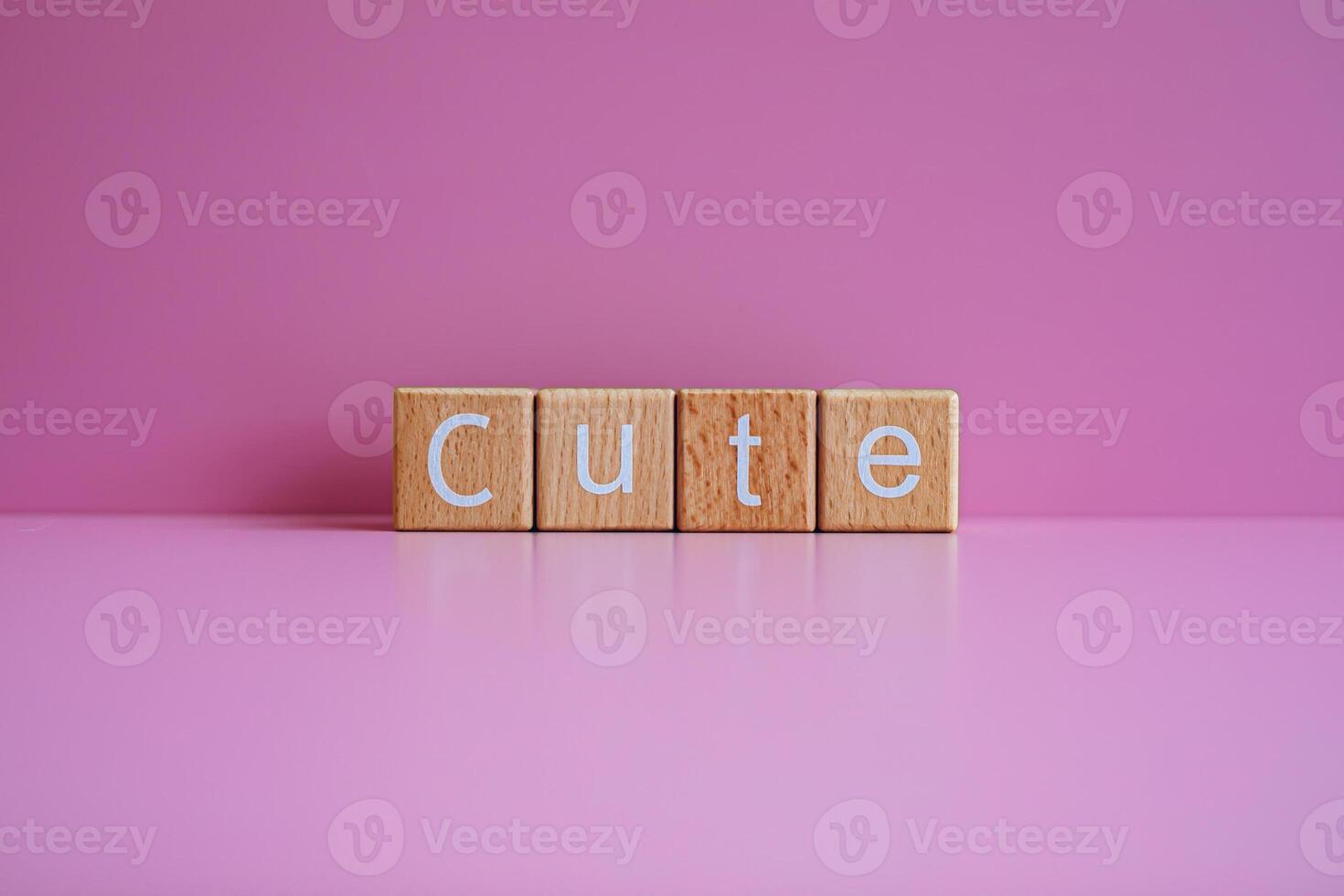 Wooden blocks form the text Cute against a pink background. photo