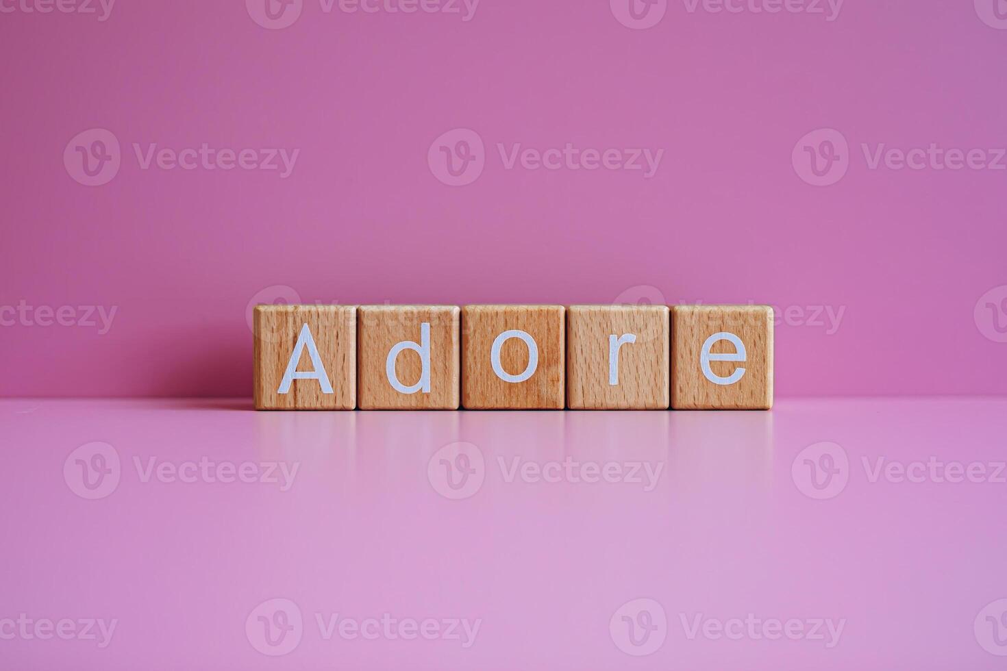 Wooden blocks form the text Adore against a pink background. photo