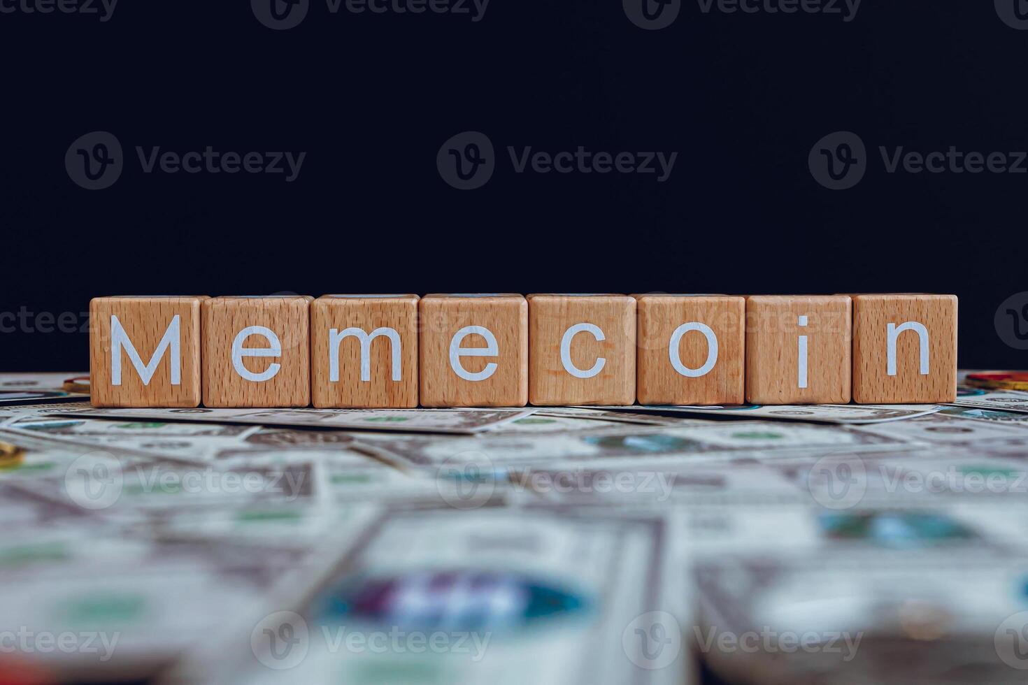 Wooden blocks with the text Memecoin on a black background and crypto banknotes scattered on the ground. photo