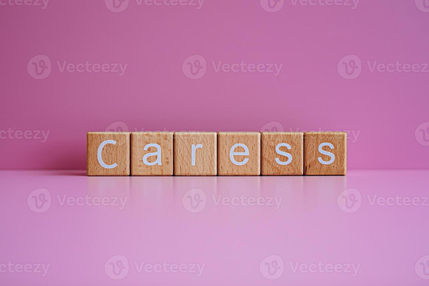 Wooden blocks form the text Caress against a pink background. photo