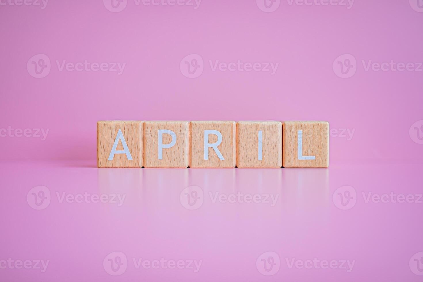 Wooden blocks form the text APRIL against a pink background. photo