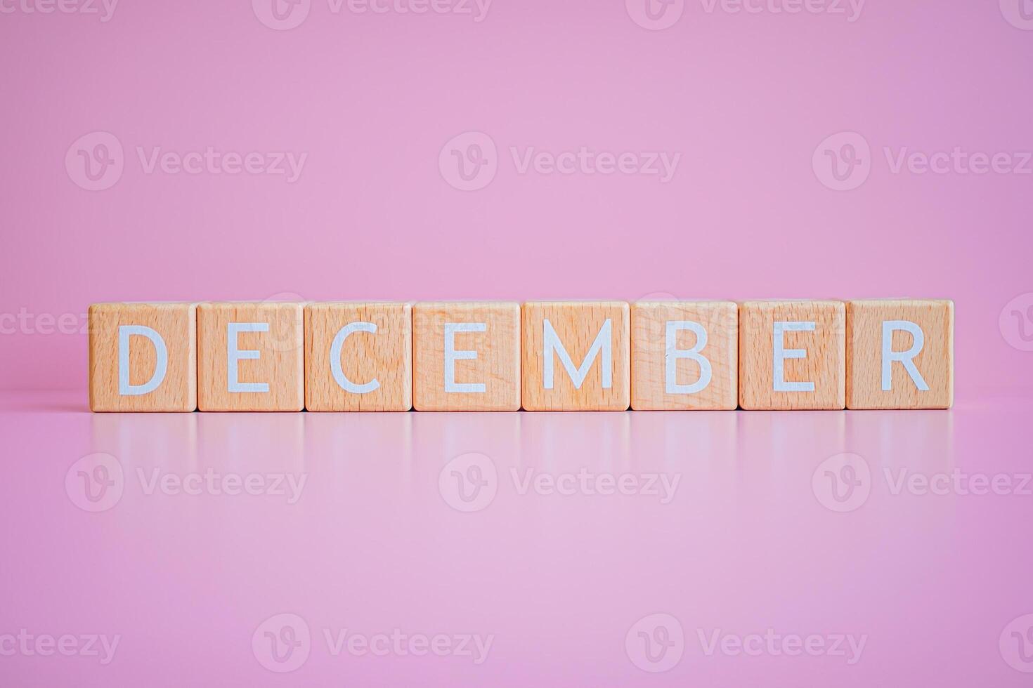 Wooden blocks form the text DECEMBER against a pink background. photo