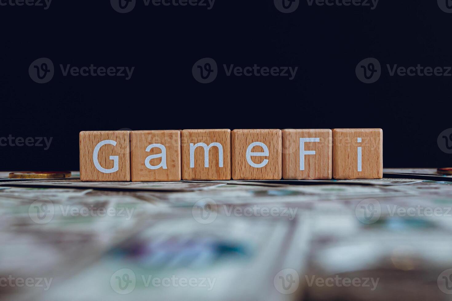 Wooden blocks with the text GameFi on a black background and crypto banknotes scattered on the ground. photo
