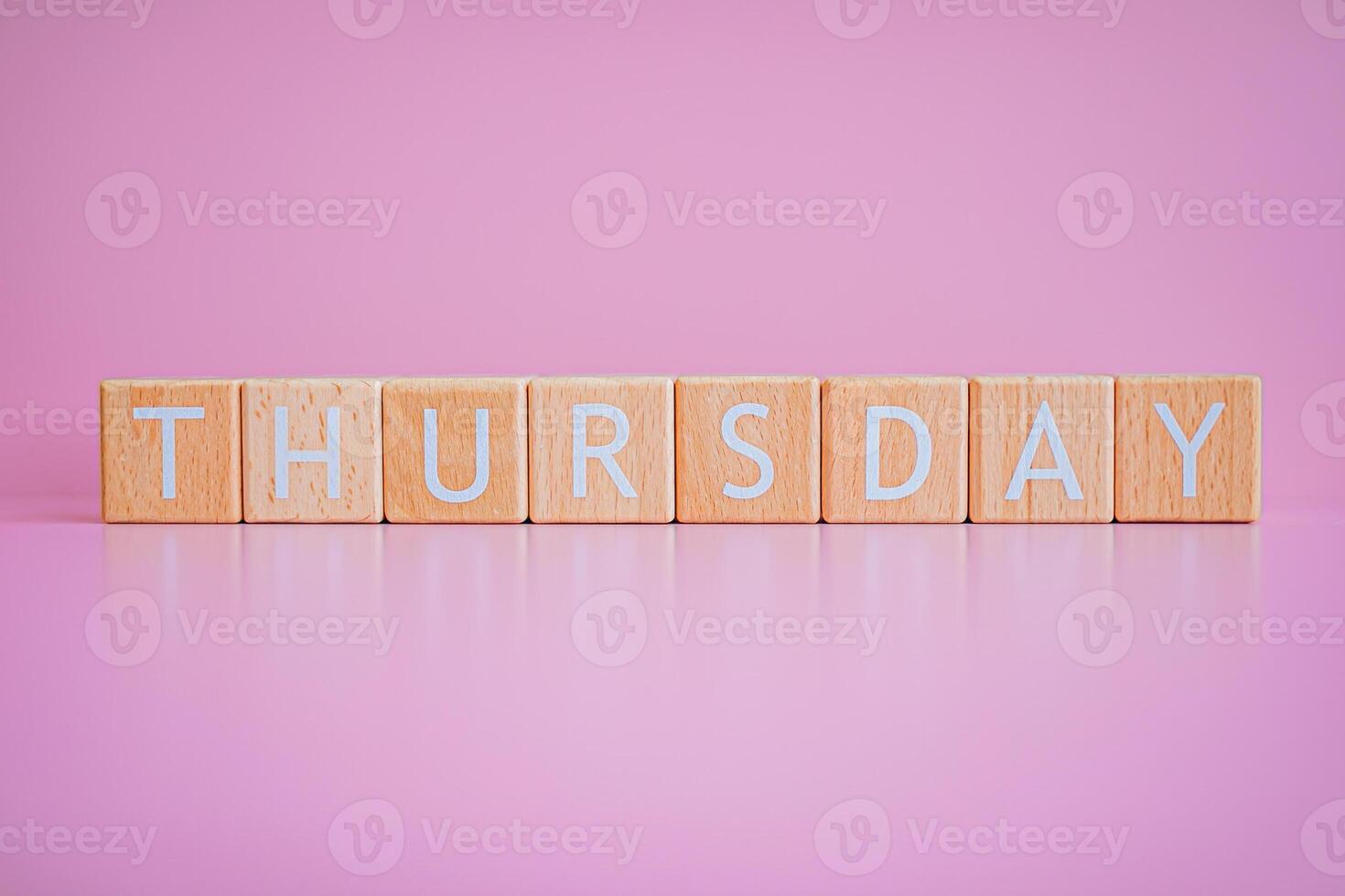 Wooden blocks form the text THURSDAY against a pink background. photo