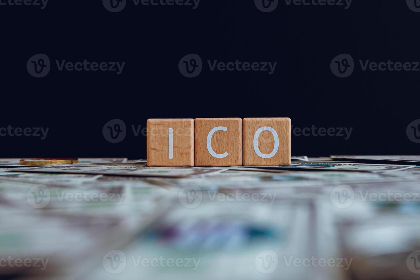 de madera bloques con el texto ico en un negro antecedentes y cripto billetes dispersado en el suelo. foto