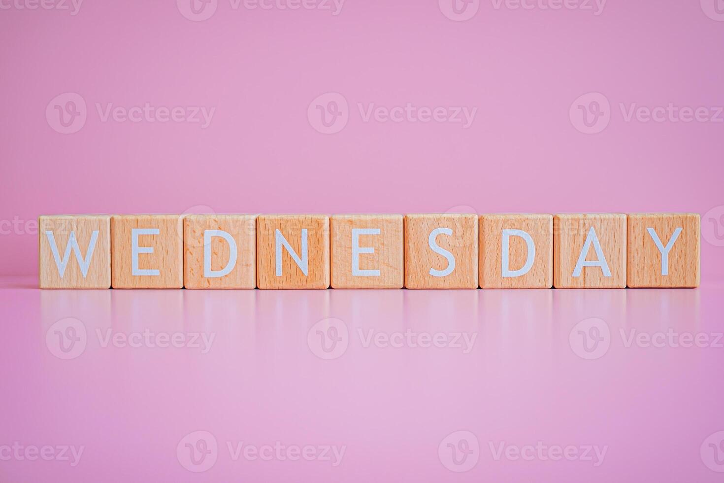 Wooden blocks form the text WEDNESDAY against a pink background. photo