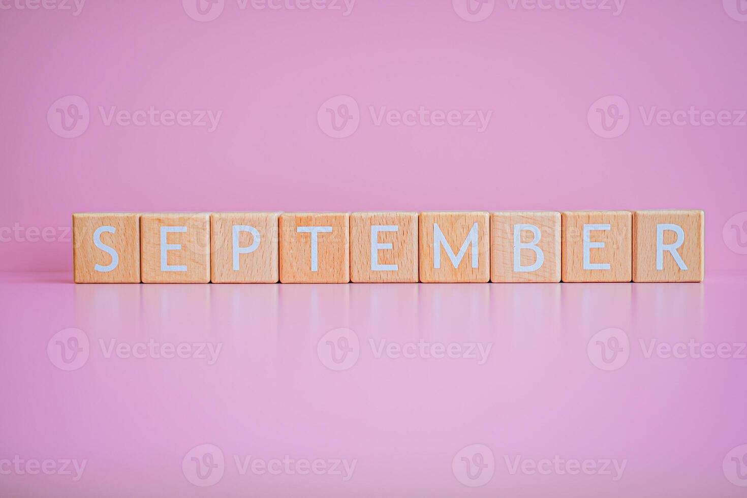 Wooden blocks form the text SEPTEMBER against a pink background. photo