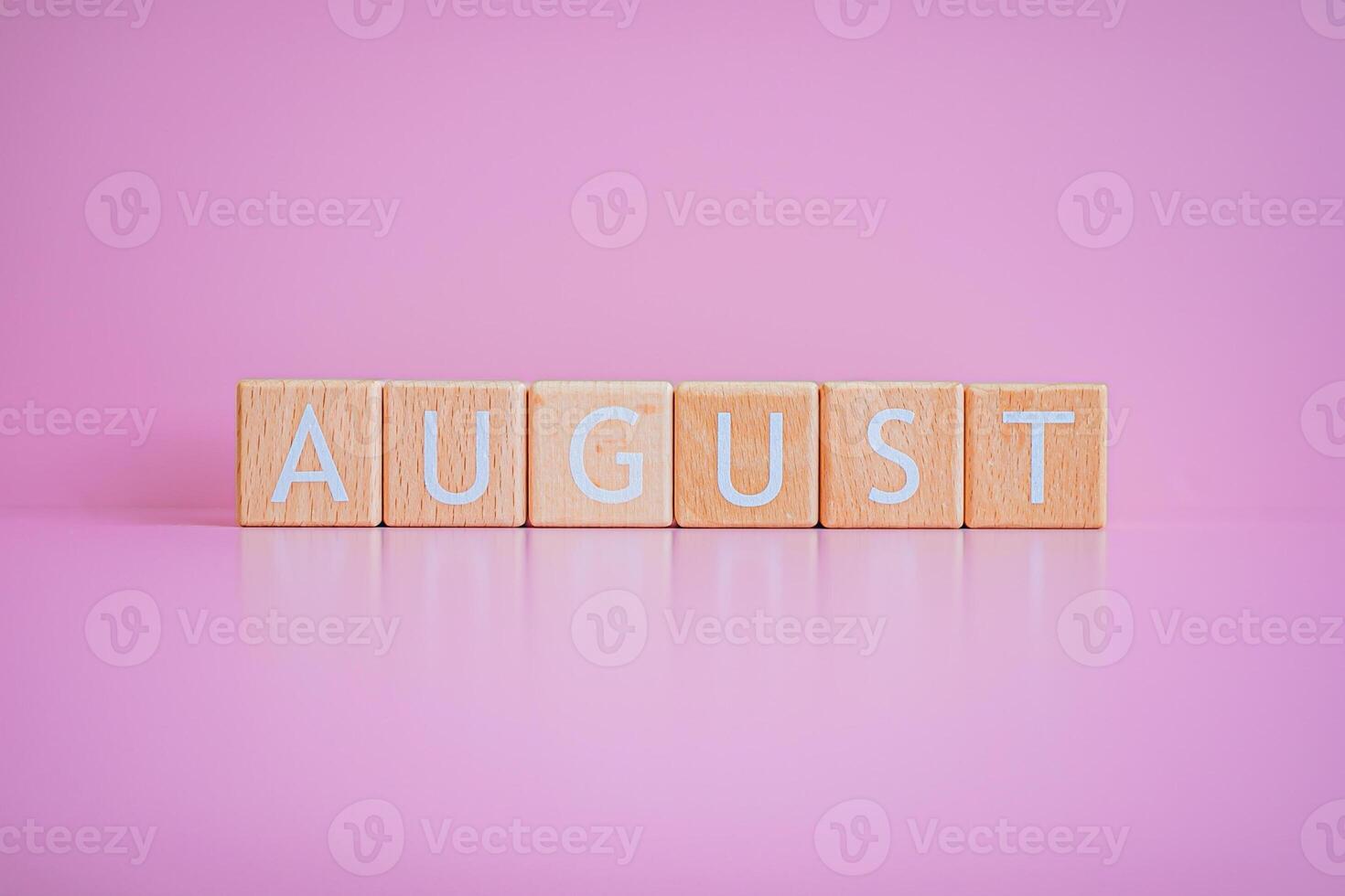 Wooden blocks form the text AUGUST against a pink background. photo