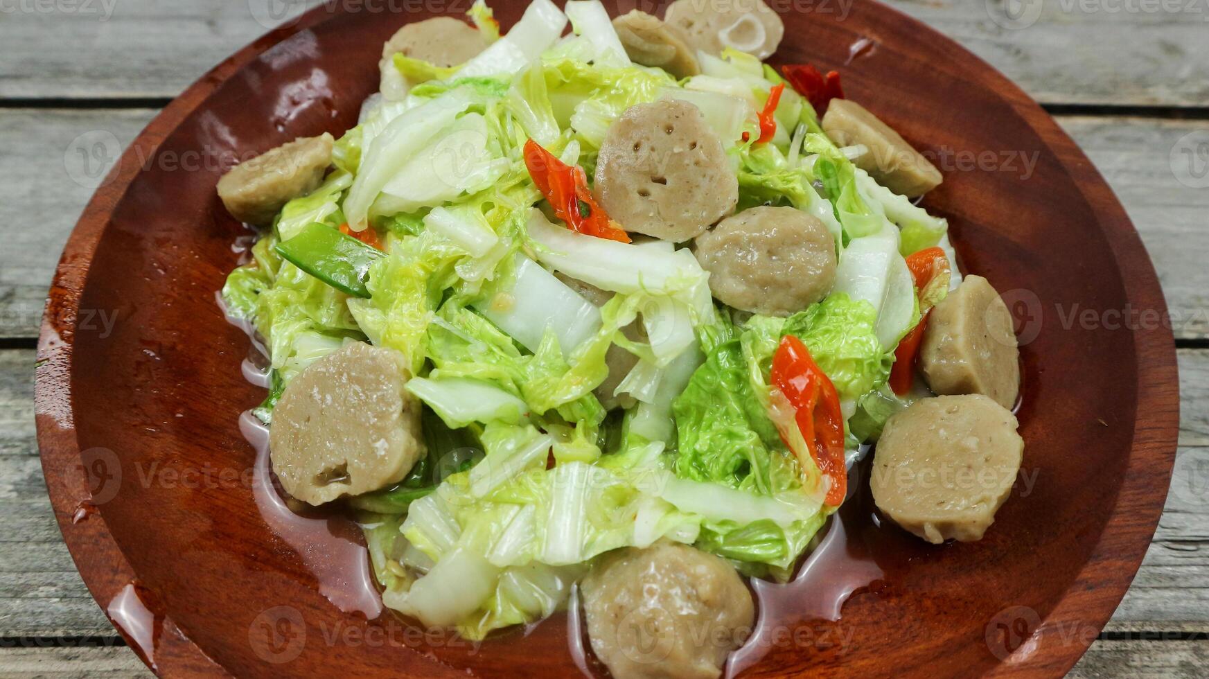 Indonesian cuisine, Tumis napa cabbage - Indonesian Spicy stir fry napa cabbage with meatball, typical Indonesian daily homedish, served in white bowl over brown wooden background photo