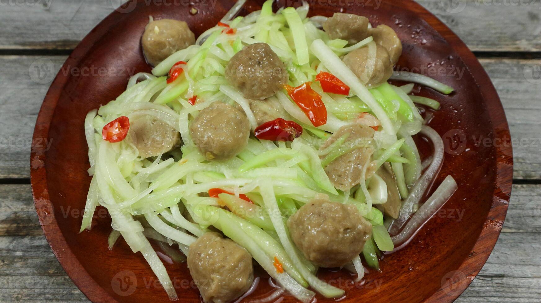 Indonesian cuisine, Tumis labu siam - Indonesian Spicy stir fry chayote with meatball, typical Indonesian daily homedish, served in white bowl over brown wooden background photo