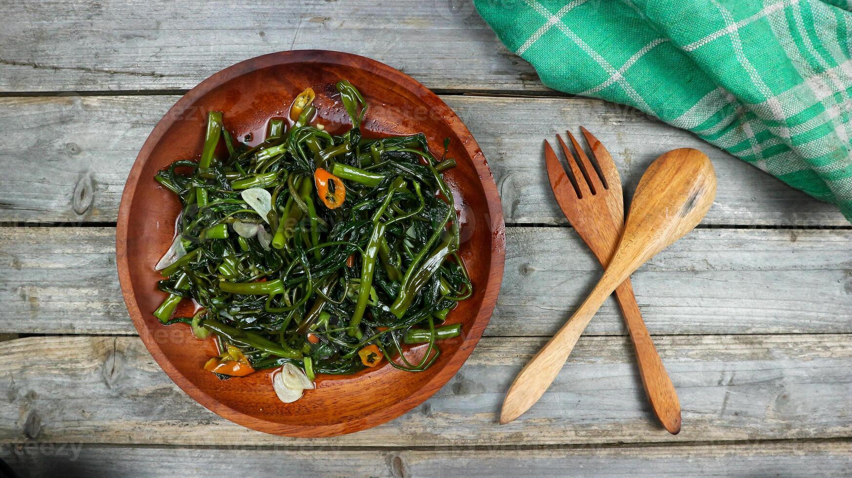 Stir fried water spinach or tumis kangkung indonesian food served on wooden plate and isolated on wooden grey table. Selective Focus. Top view. Closeup. Copy space for text photo