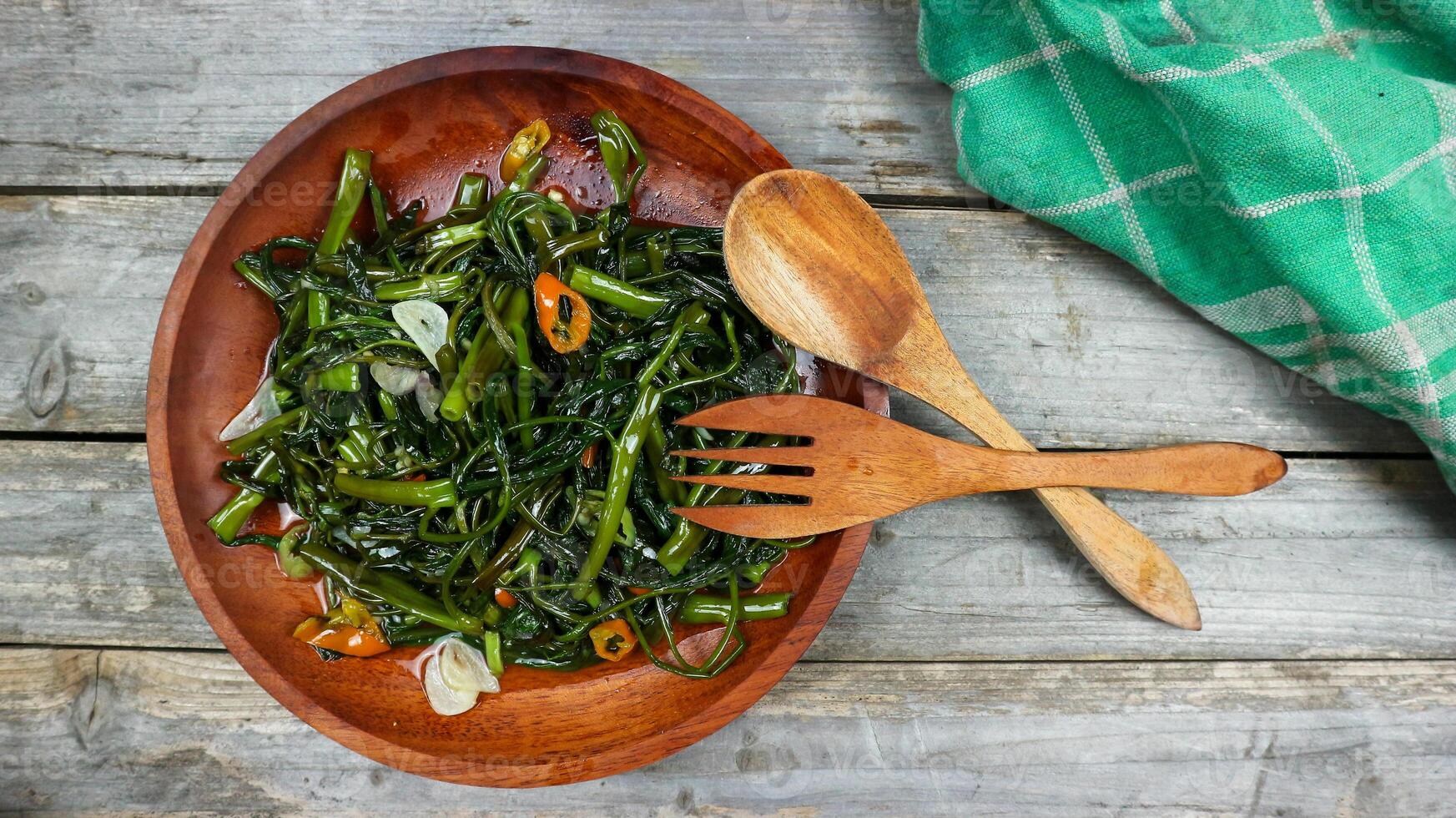 Stir fried water spinach or tumis kangkung indonesian food served on wooden plate and isolated on wooden grey table. Selective Focus. Top view. Closeup. Copy space for text photo