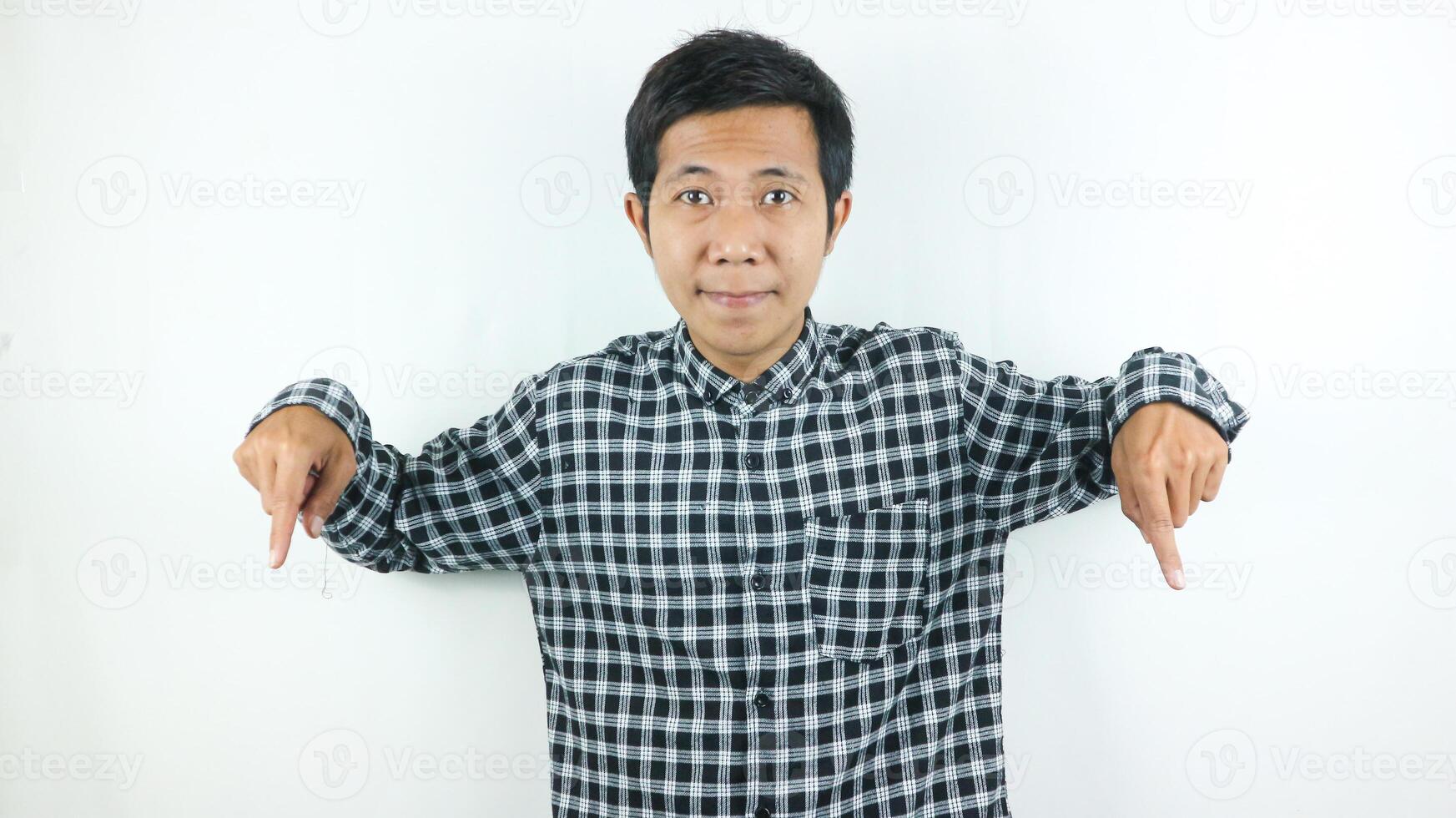 Adult Asian man wearing plaid shirt smiling while looking and pointing below. photo