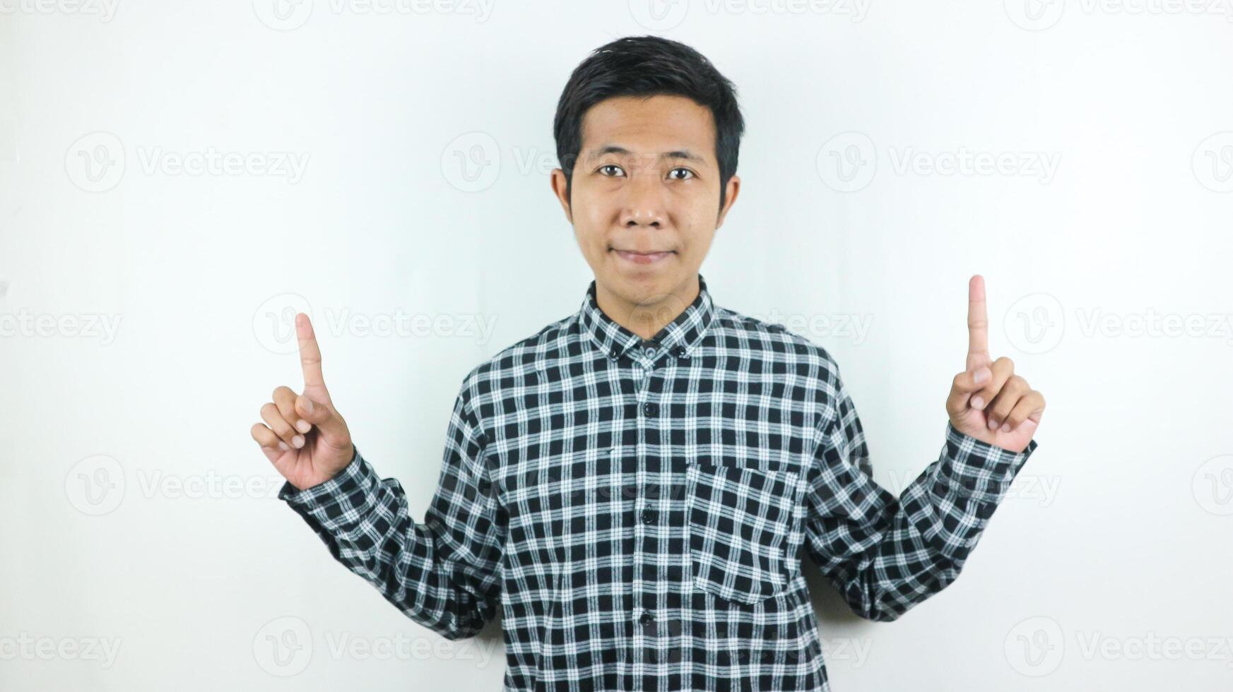 Adult Asian man wearing plaid shirt smiling while looking and pointing up side. photo