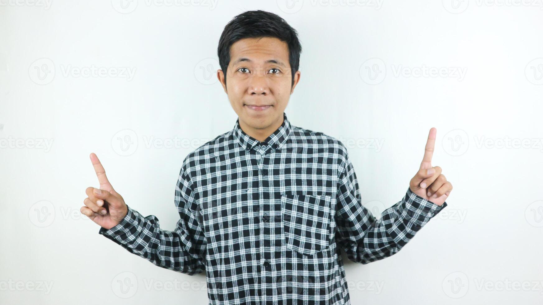 Adult Asian man wearing plaid shirt smiling while looking and pointing up side. photo