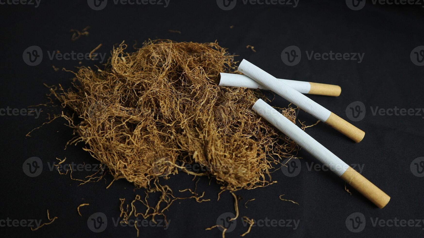 dry cut tobacco leaf, cigarettes and cigarette machine on black background. handmade cigarettes photo