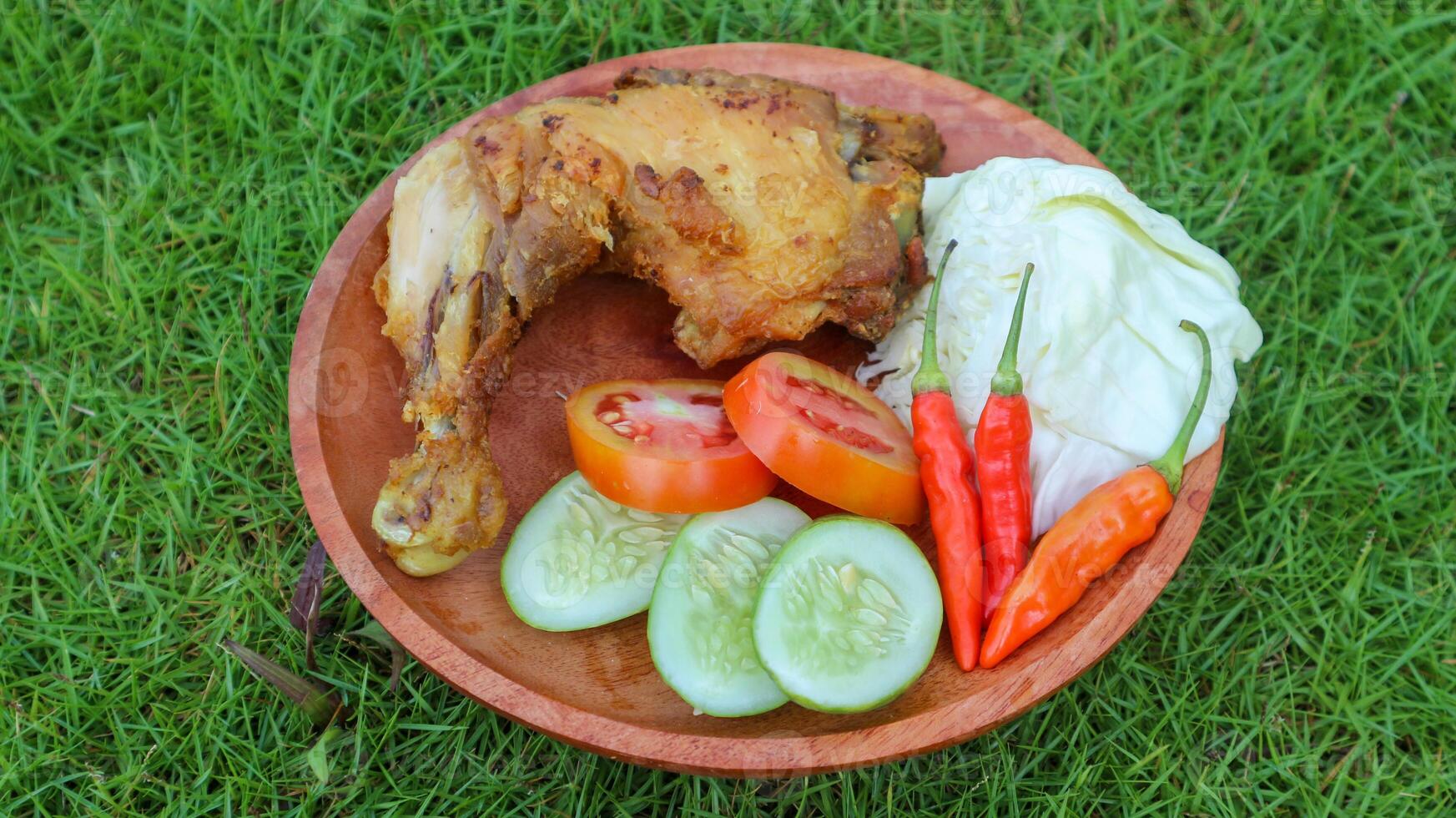 frito pollo con lalapan, frito pollo con Fresco verduras, tomate rebanadas, Pepino y sambal auténtico receta de indonesio pollo lalapán. frito pollo en verde césped antecedentes. foto