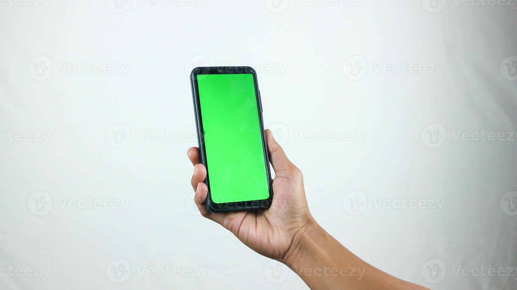 Asian man holding big smartphone with white, red, green, blue blank screen in hand, showing close to camera and pointing at device. Gadget with empty free space for mock up, banner photo