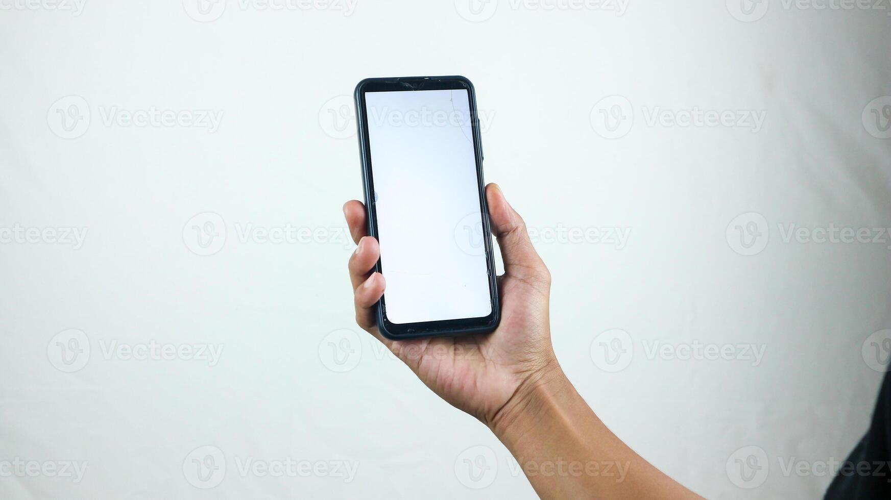 Asian man holding big smartphone with white, red, green, blue blank screen in hand, showing close to camera and pointing at device. Gadget with empty free space for mock up, banner photo