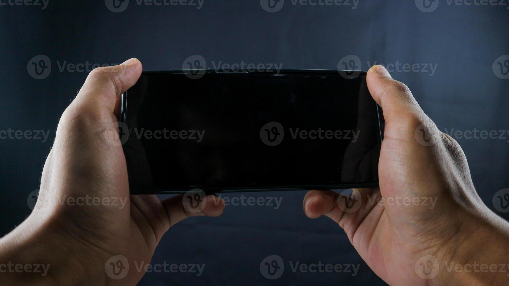 Hand holding cell phone look like playing a game blank on black screen and black background photo