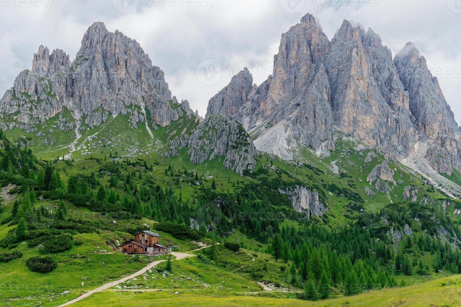 Rifugio Citta Di Carpi, Mountain Hut, with Cadini di Misurina mountains in the background in the Dolomites, Italy. Green vegetation and clouds in the sky. photo