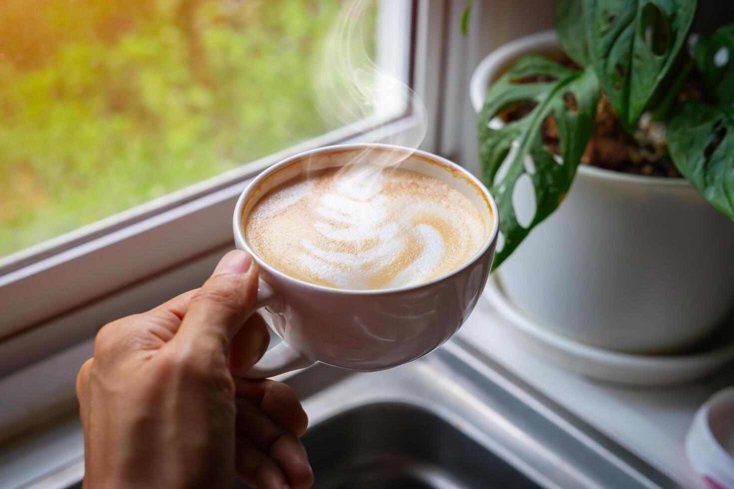person's hand is holding an aromatic latte art coffee cup. Drink coffee on the morning near the window photo