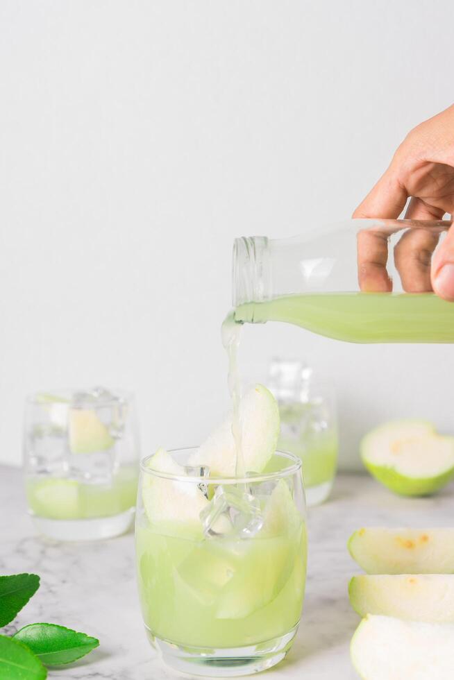 mano personas son torrencial guayaba jugo desde un botella sobre un vaso. frio refrescante Fruta jugo salud beber. vertical foto