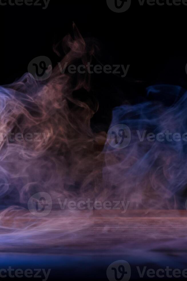 imagen conceptual de humo multicolor aislado sobre fondo negro oscuro y mesa de madera. foto