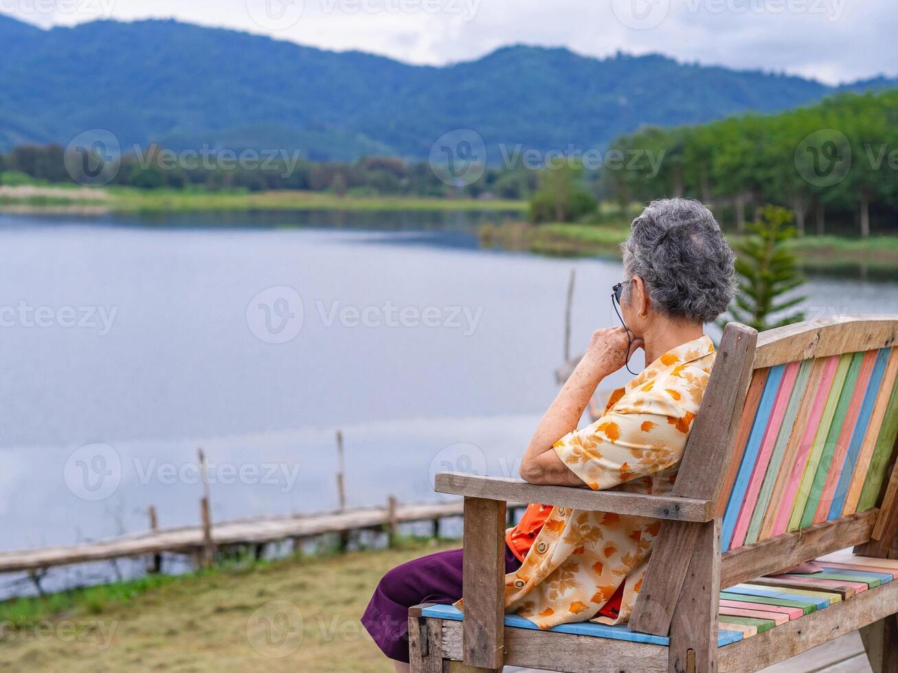 Side view of a senior woman while sitting on chairside the lake. photo