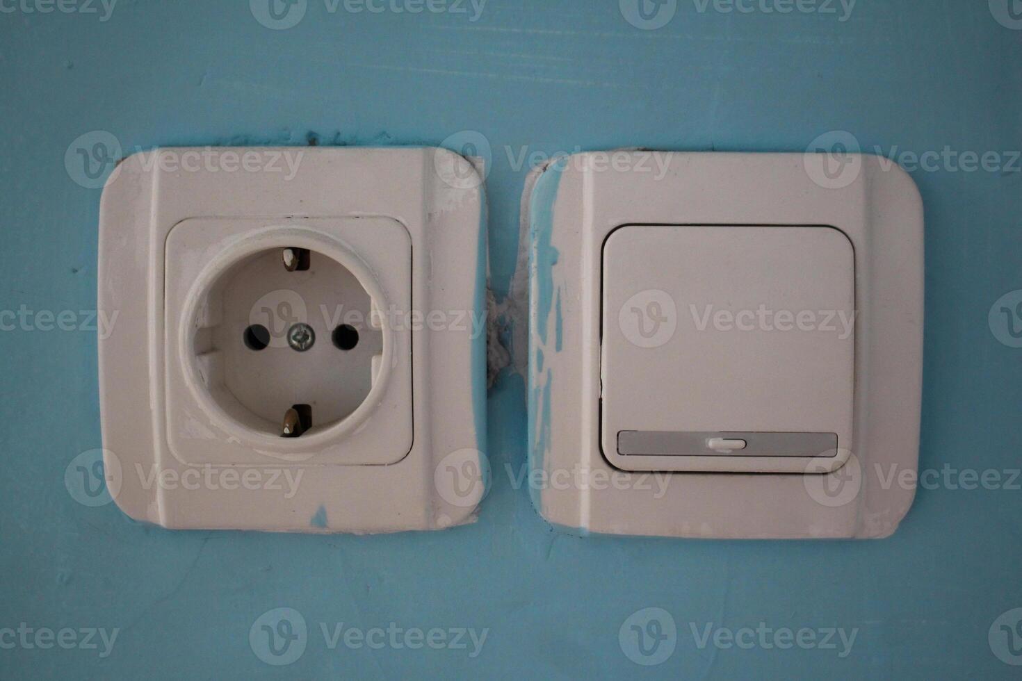 The white wall light switch and socket socket are slightly stained with paint on the blue wall photo