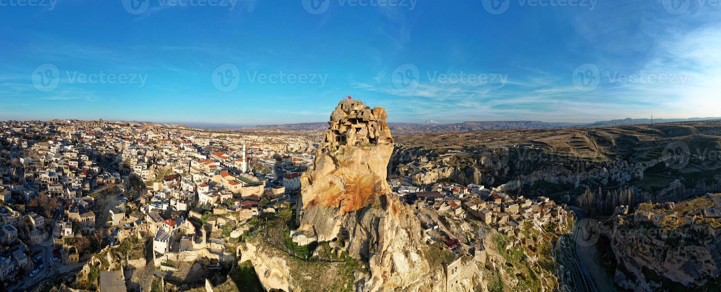 Aerial drone view of the Ortahisar Castle in Cappadocia, Turkey with the snow capped Mount Erciyes in the background. People enjoying the view from the top of the castle. photo