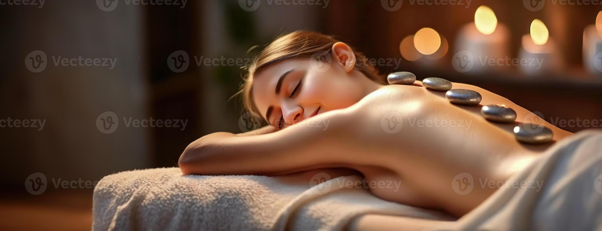 AI Generated Relaxing Spa Day with Hot Stone Therapy. A serene woman enjoys massage, candles flickering in the peaceful atmosphere. Panorama with copy space. photo