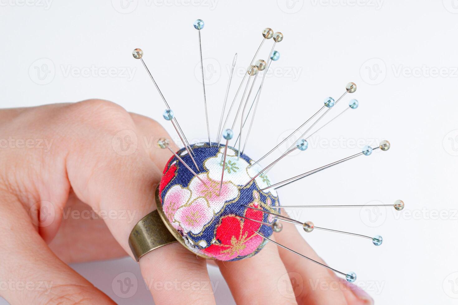 a ring with a small pillow for needles on a hand on a white background photo