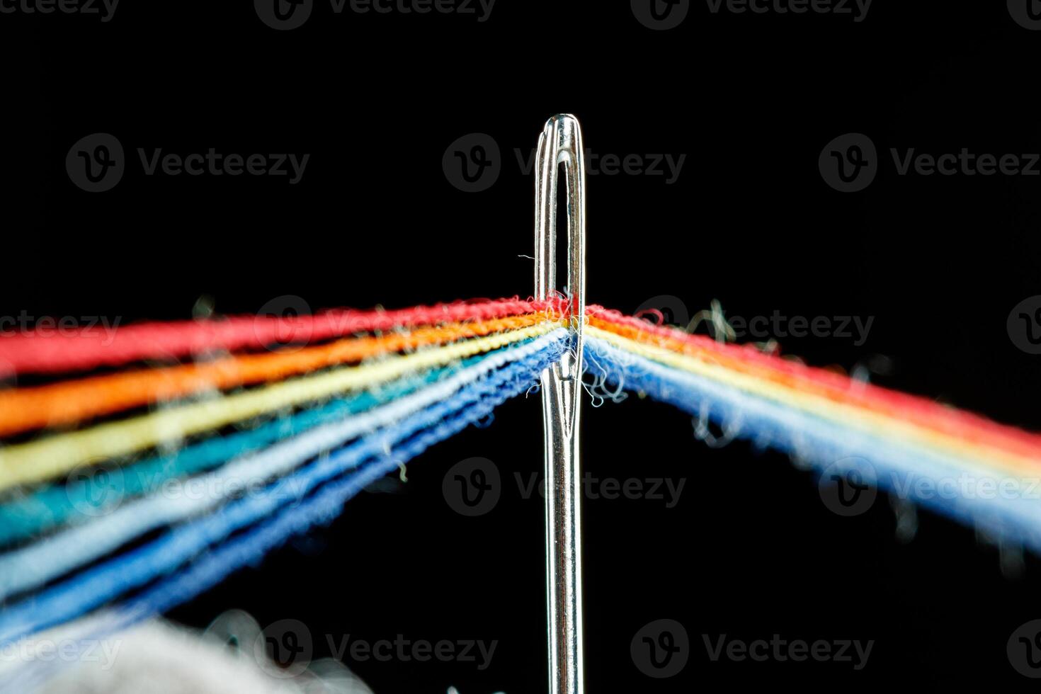 multi-colored threads for sewing in the form of a rainbow pass through an antique needle on a black background photo
