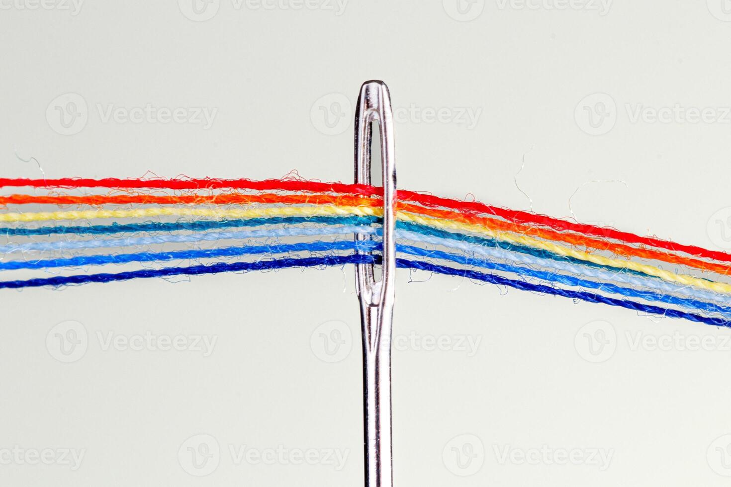 multi-colored threads for sewing in the form of a rainbow pass through an antique needle on a white background photo