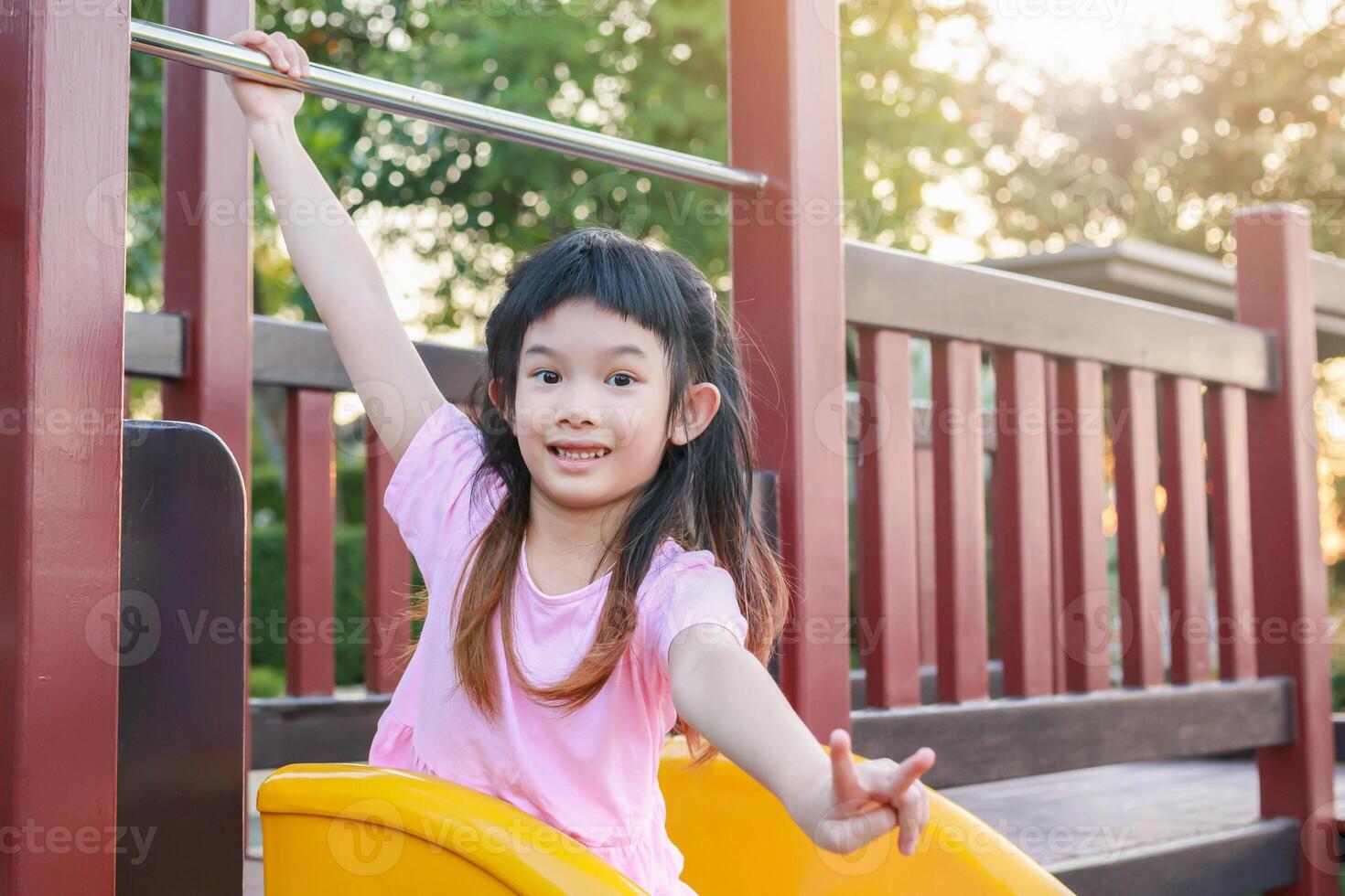 Cute asian girl playing on the slide in the playground photo