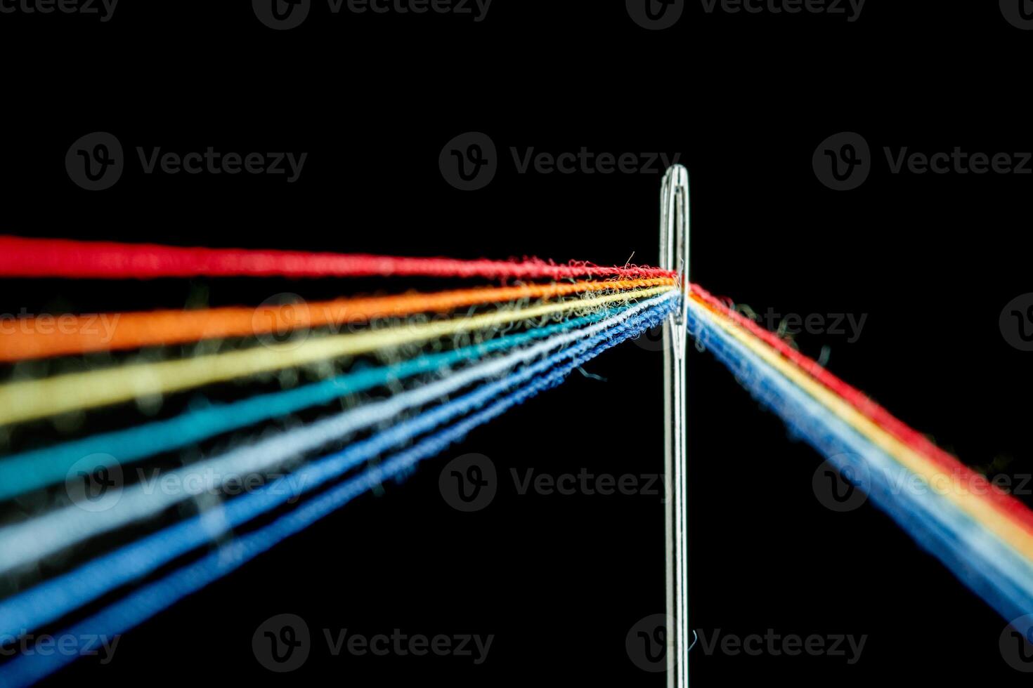 multi-colored threads for sewing in the form of a rainbow pass through an antique needle on a black background photo