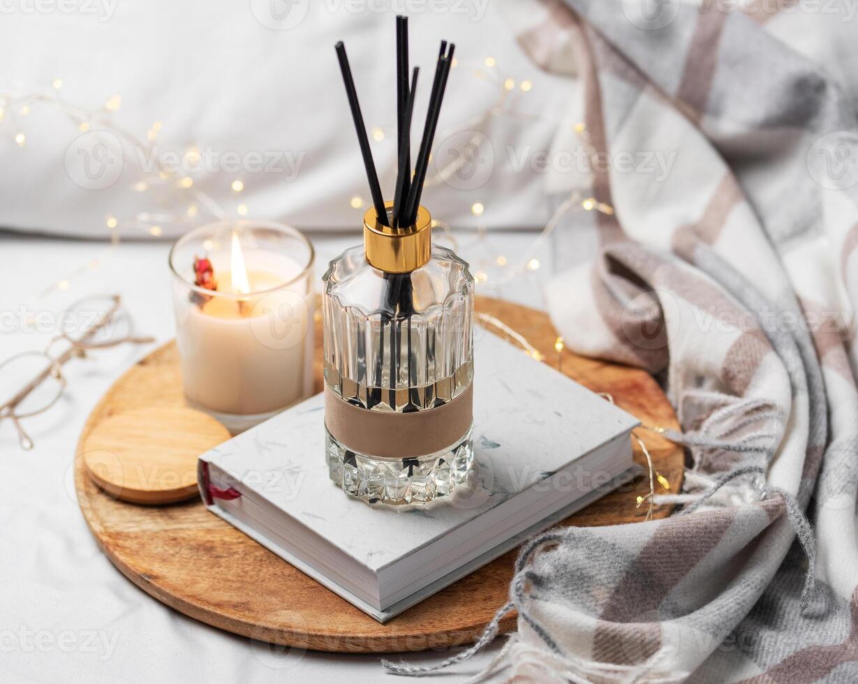 Home fragrance in glass bottle and bamboo sticks with scented candle,  paper book. photo