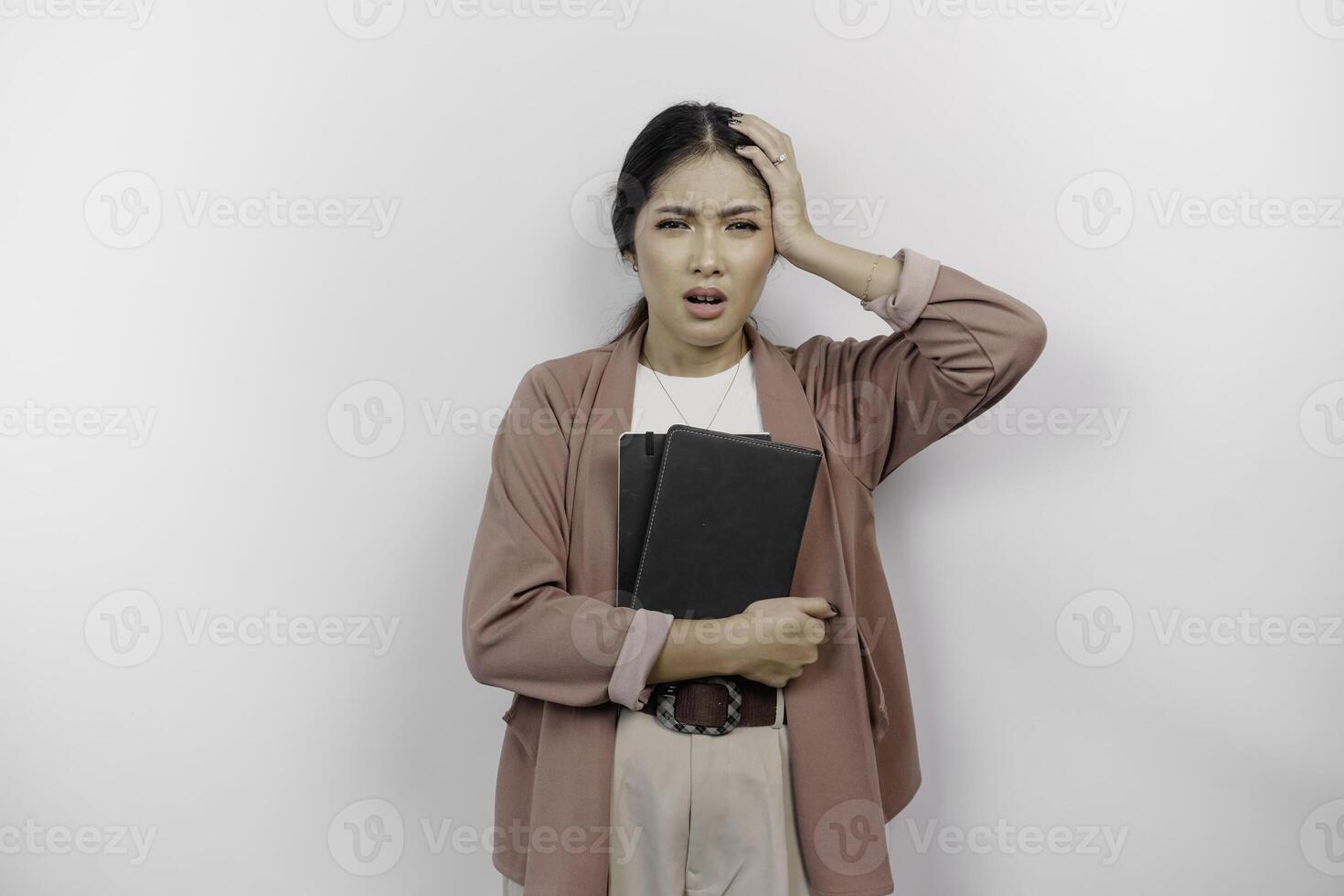 A stressed young Asian student wearing cardigan while holding books, isolated by white background. photo
