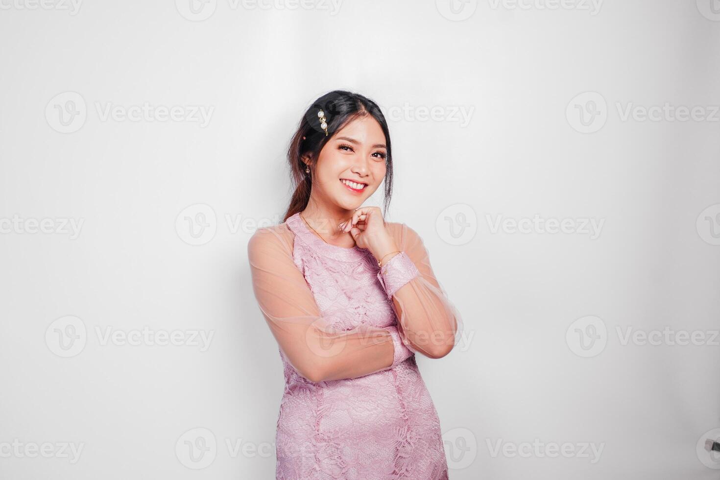 An attractive Asian woman wearing pink dress is smiling to the camera, isolated by white background. photo