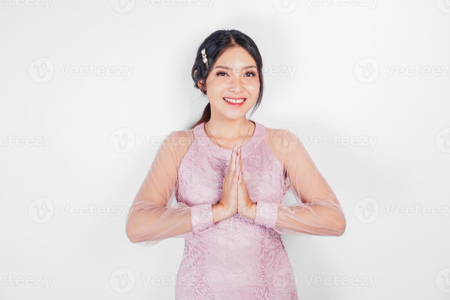 simpático asiático mujer vistiendo rosado vestir es dando gestos de tradicional saludos por su manos foto