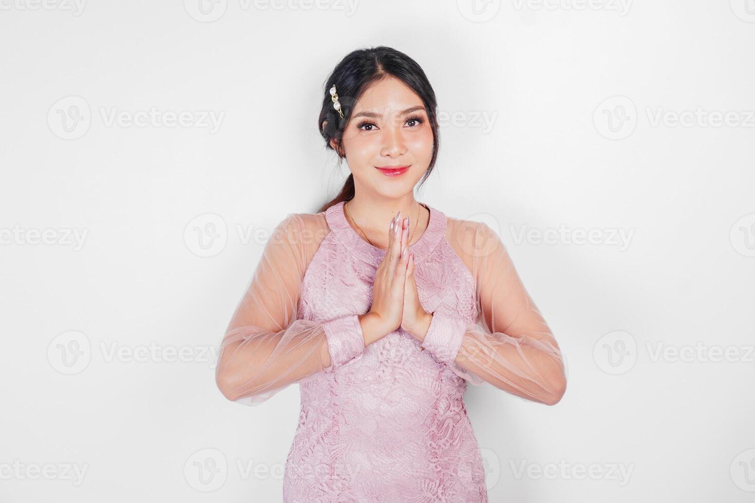 simpático asiático mujer vistiendo rosado vestir es dando gestos de tradicional saludos por su manos foto