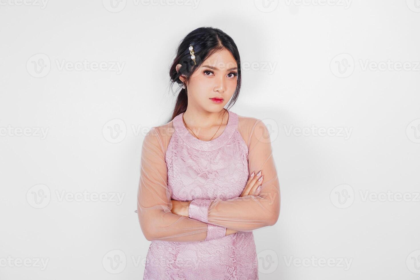un asiático joven mujer vistiendo rosado vestir es dando grave expresión mientras cruce su manos foto