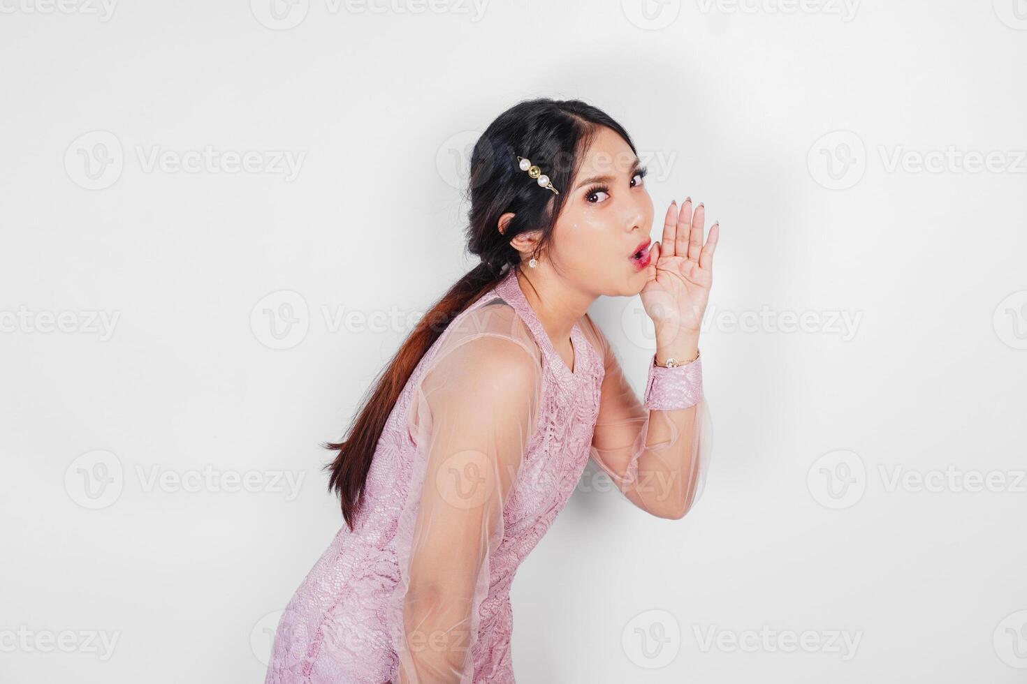 A young beautiful Asian woman is shouting and screaming loud with a hand on her mouth, isolated by white background. photo